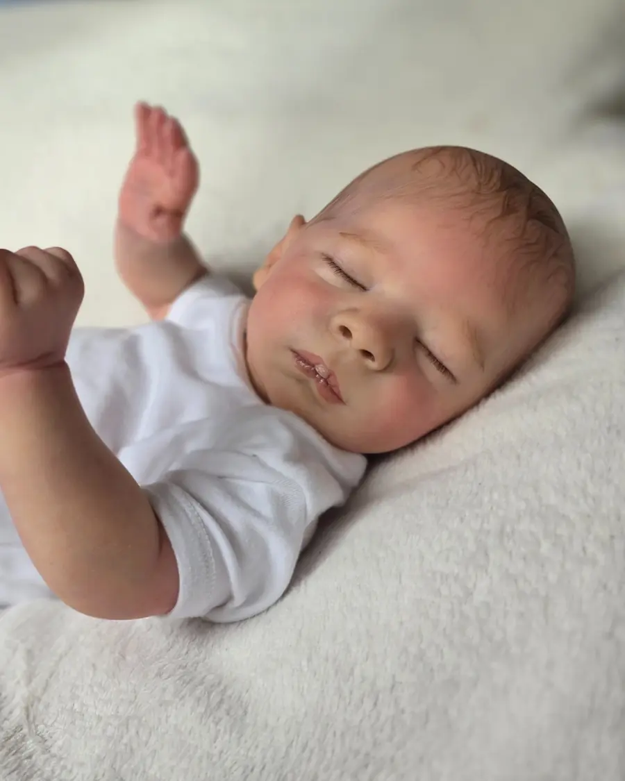 Reborn doll in a white bodysuit lying on a cream blanket.